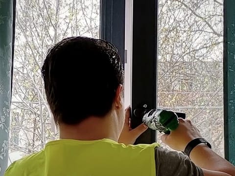 Mâinile tehnicianului lucrând la mecanismul de lângă mânerul ferestrei.